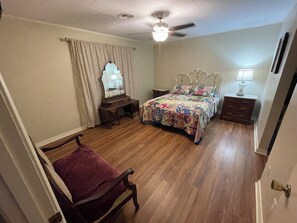 A bedroom with a bed, a vanity with a mirror, a chair, a nightstand, and a ceiling fan.