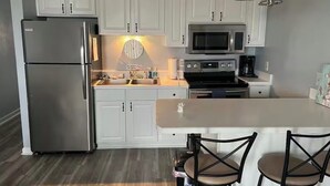 Een moderne keuken met witte kasten, roestvrijstalen apparatuur, een centraal eiland met barstoelen en een hangende lamp.