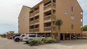 Een hotel met meerdere verdiepingen, balkons, een parkeerplaats en een palmboom.