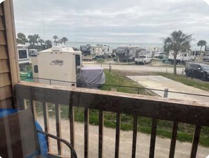 Blick auf einen Campingplatz mit Wohnmobilen und Wohnwagen, einem eingezäunten Bereich und einem Strand im Hintergrund.