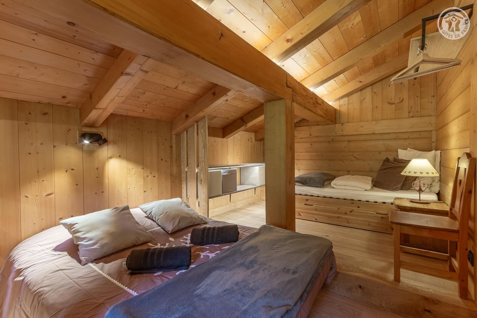 L’intérieur d’une cabane en bois, avec un lit, un banc, une table et un luminaire suspendu.