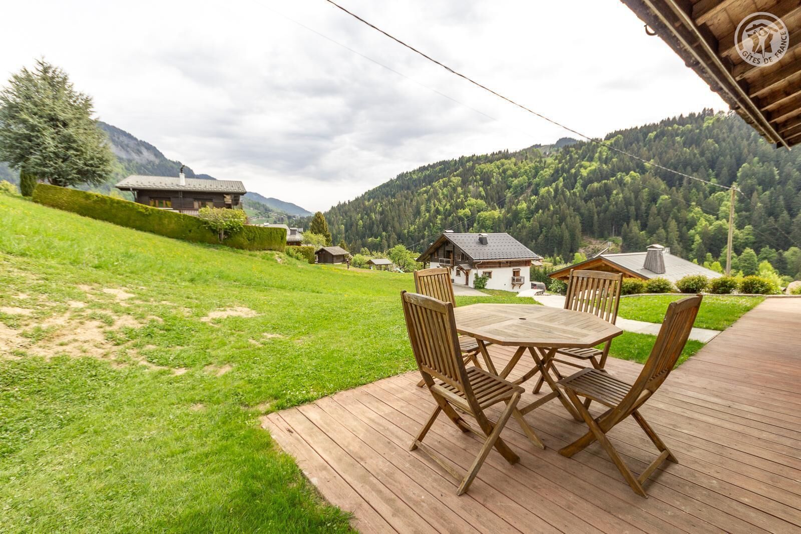 Une terrasse en bois avec une table et des chaises, offrant une vue sur un paysage montagneux parsemé de maisons.