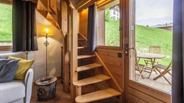 A wooden interior with a staircase, a sofa, a lamp, and a view of the outdoors. - Le Petit Riondet - SAINT NICOLAS LA CHAPELLE (SAINT NICOLAS LA CHAPELLE)