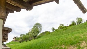 A wooden deck leading to a building with a sloped roof, a grassy hill in the background, and a stone wall. - Le Petit Riondet - SAINT NICOLAS LA CHAPELLE (SAINT NICOLAS LA CHAPELLE)