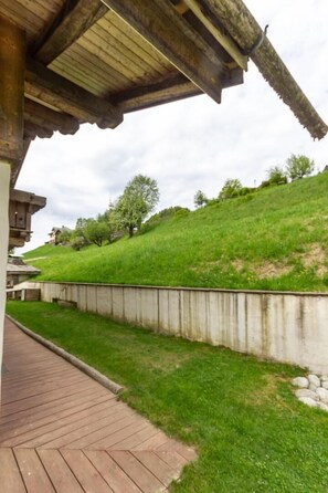 A wooden deck leading to a building with a sloped roof, a grassy hill in the background, and a stone wall. - Le Petit Riondet - SAINT NICOLAS LA CHAPELLE (SAINT NICOLAS LA CHAPELLE)