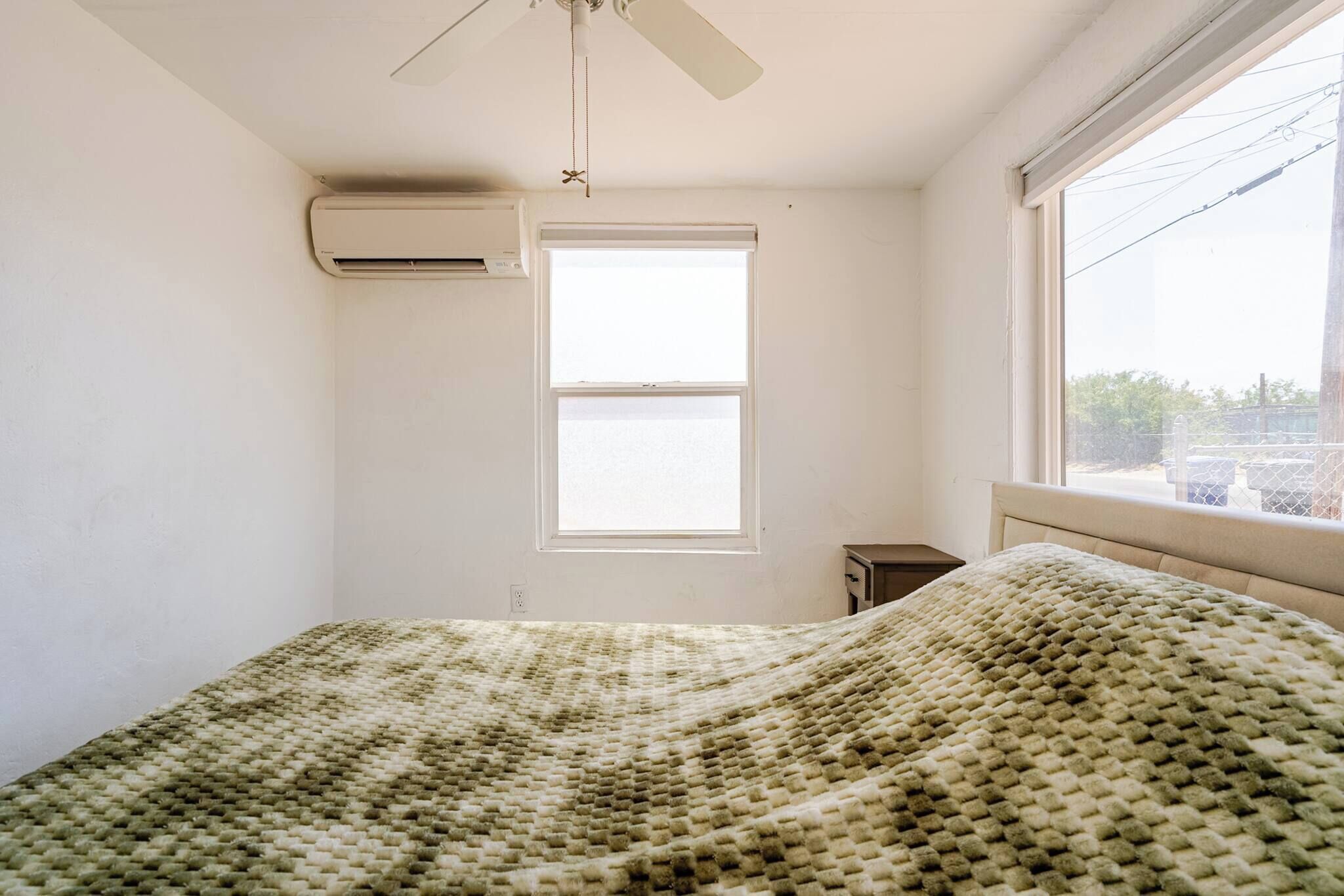 A room with a bed, an air conditioning unit, a window, and a ceiling fan.