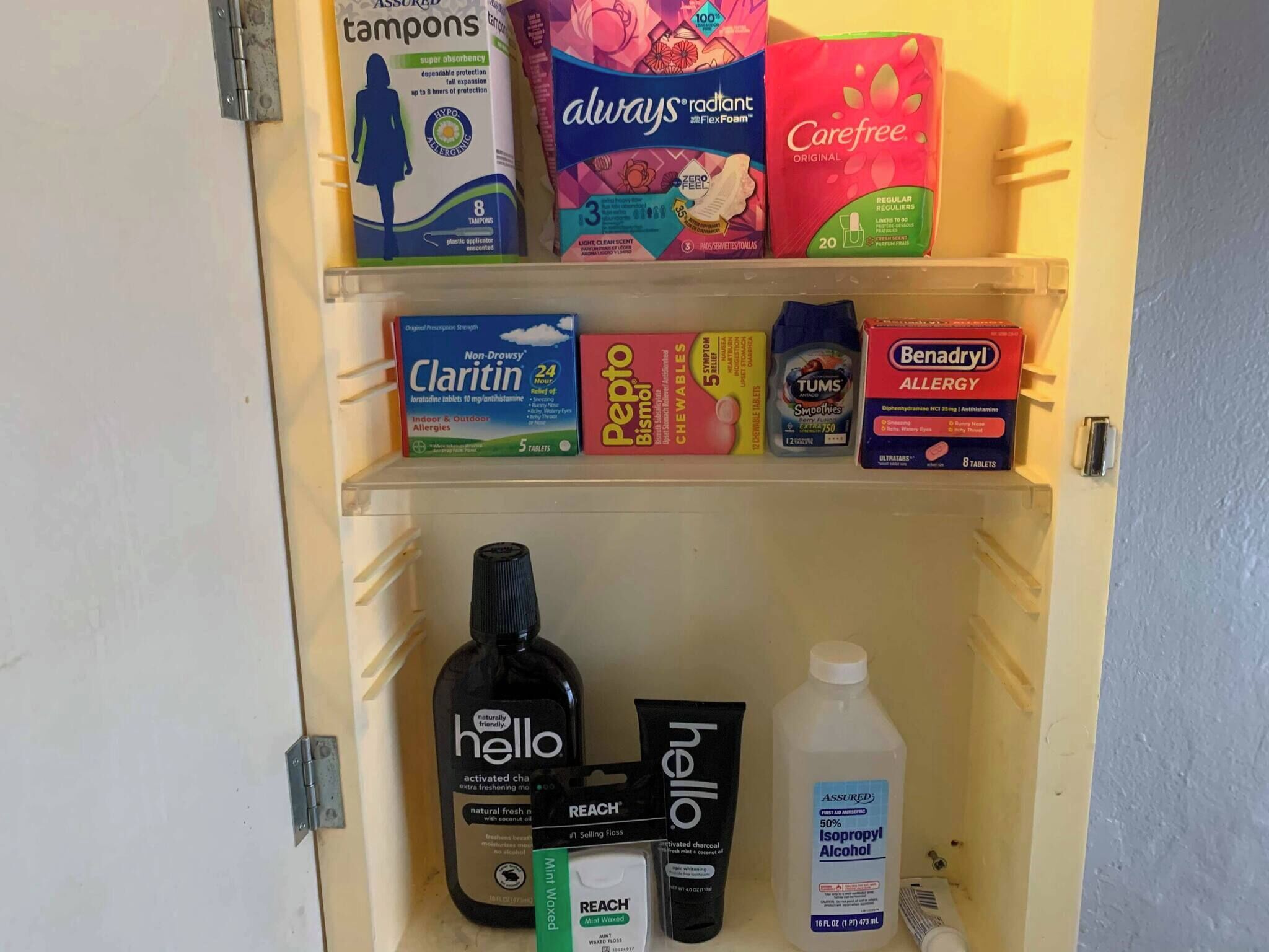 Un meuble de rangement pour médicaments contenant divers produits d’hygiène et de santé, notamment des tampons, des protections hygiéniques, des médicaments contre les allergies et des produits de soins personnels.
