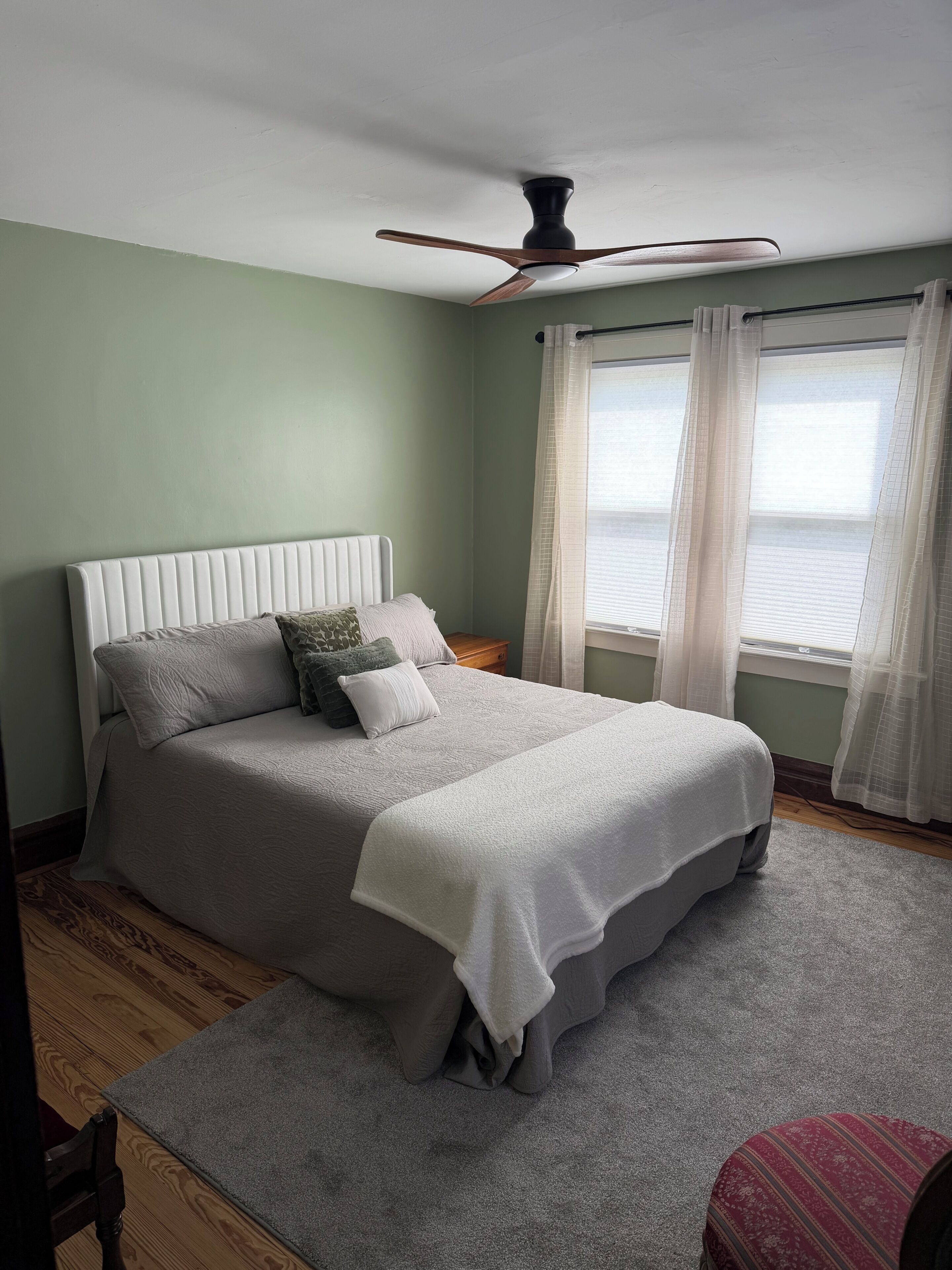 Une chambre à coucher avec un lit, un ventilateur de plafond, une fenêtre avec des rideaux et une vue sur l’extérieur.