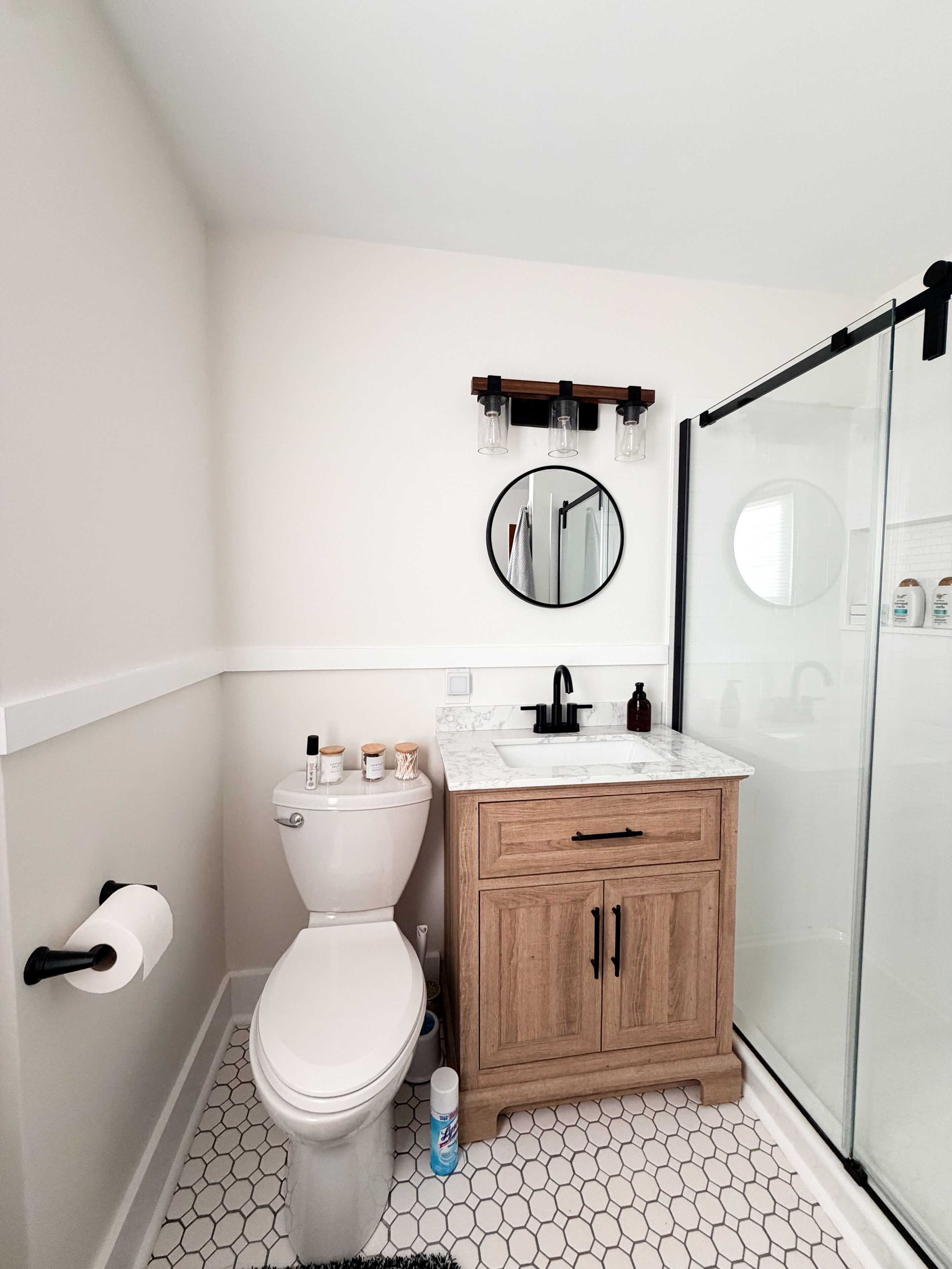 Een badkamer met toilet, een houten wastafelmeubel met een wastafel, een spiegel en een douche.