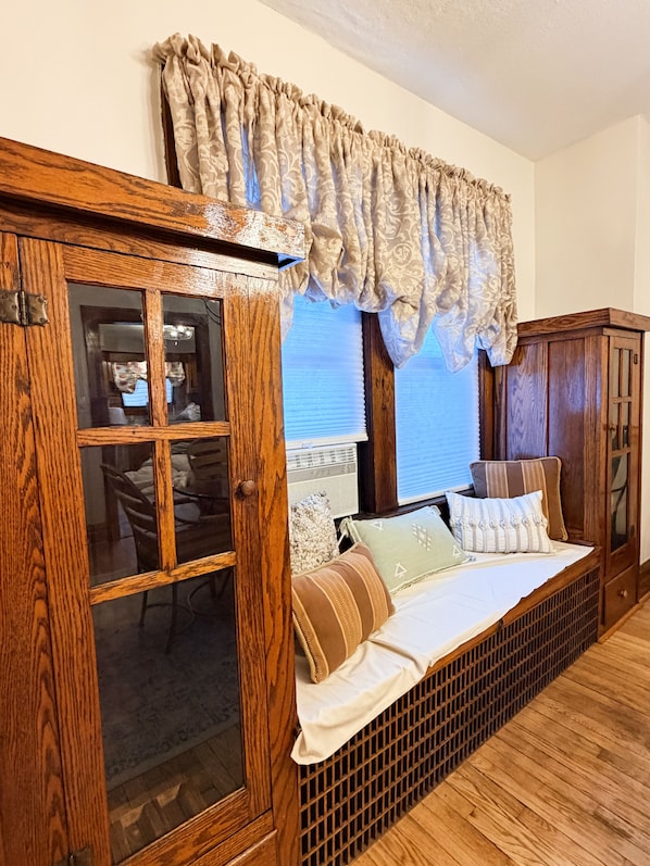A room with a wooden bench, a window with curtains, and a wooden cabinet.