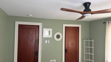 A room with two wooden doors, a ceiling fan, a white shelf, and a vent on the wall.