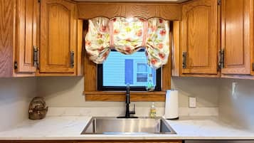 A kitchen with wooden cabinets, a stainless steel sink, and a window with floral curtains.
