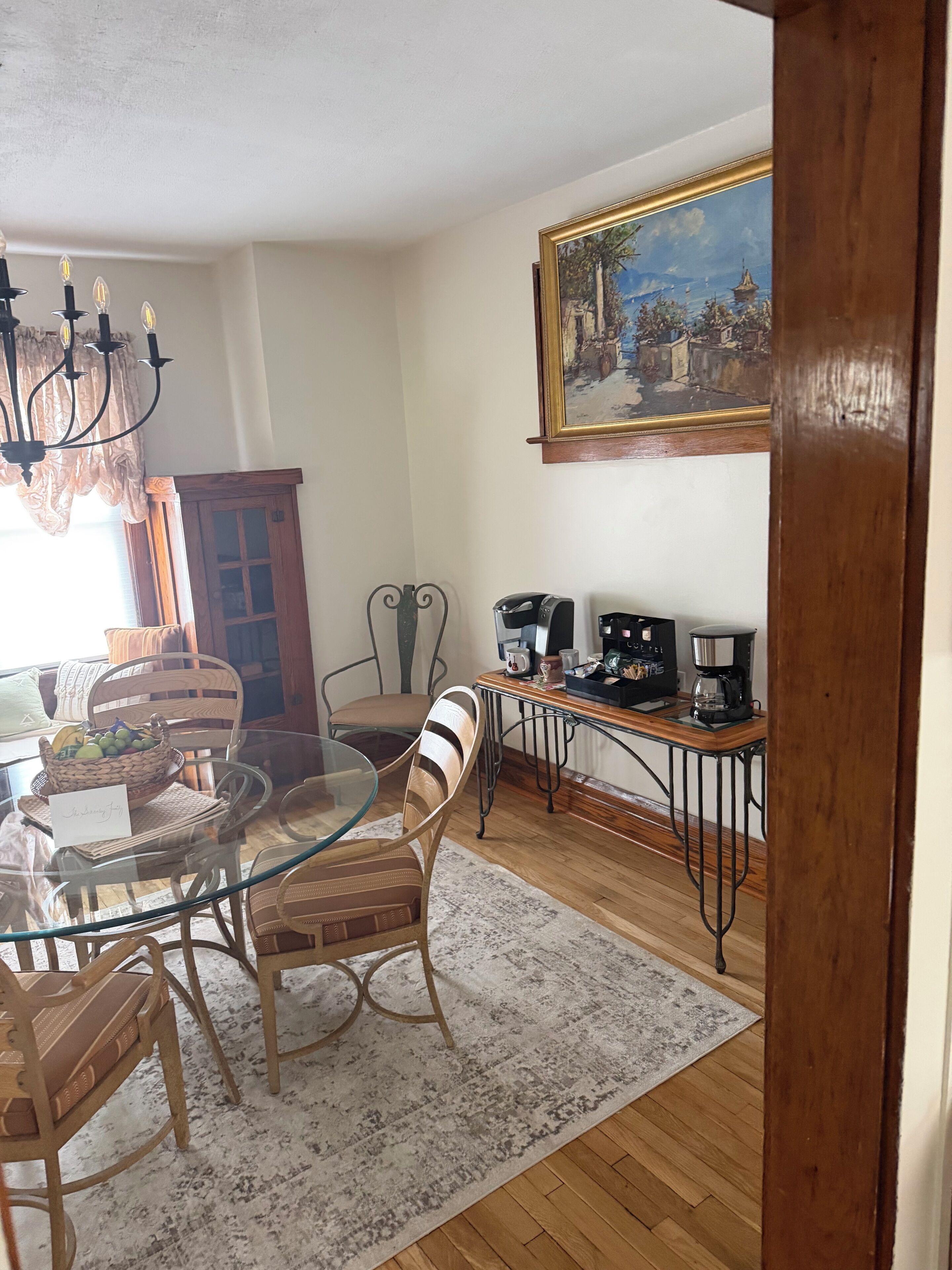 Un coin repas avec une table en verre, des chaises en osier, un espace dédié au café et un tableau accroché au mur.