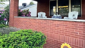 Une maison avec une façade en briques, un porche couvert et une fenêtre devant laquelle se trouve une chaise blanche.