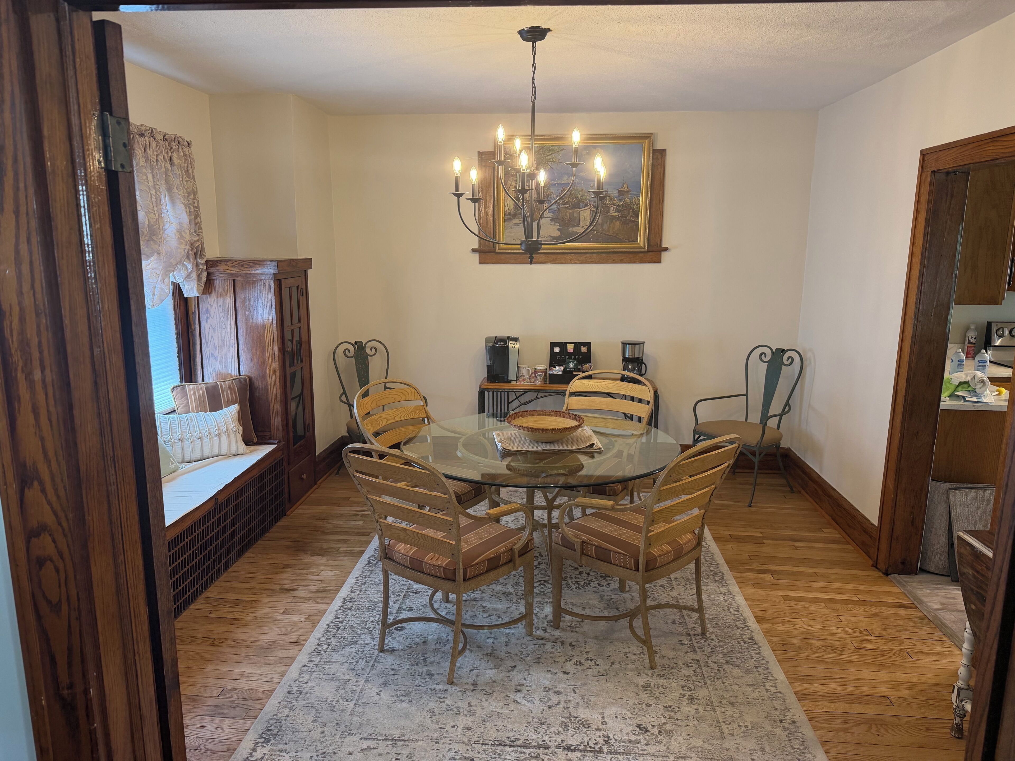 A dining area with a glass table, wooden chairs, a chandelier, and a coffee station.