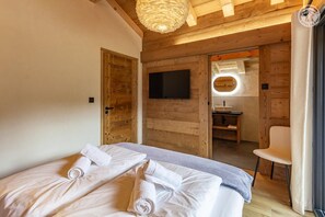 Ein Zimmer mit Holzboden, einem Bett, einem Fernseher, einem Spiegel und einem Badezimmer.