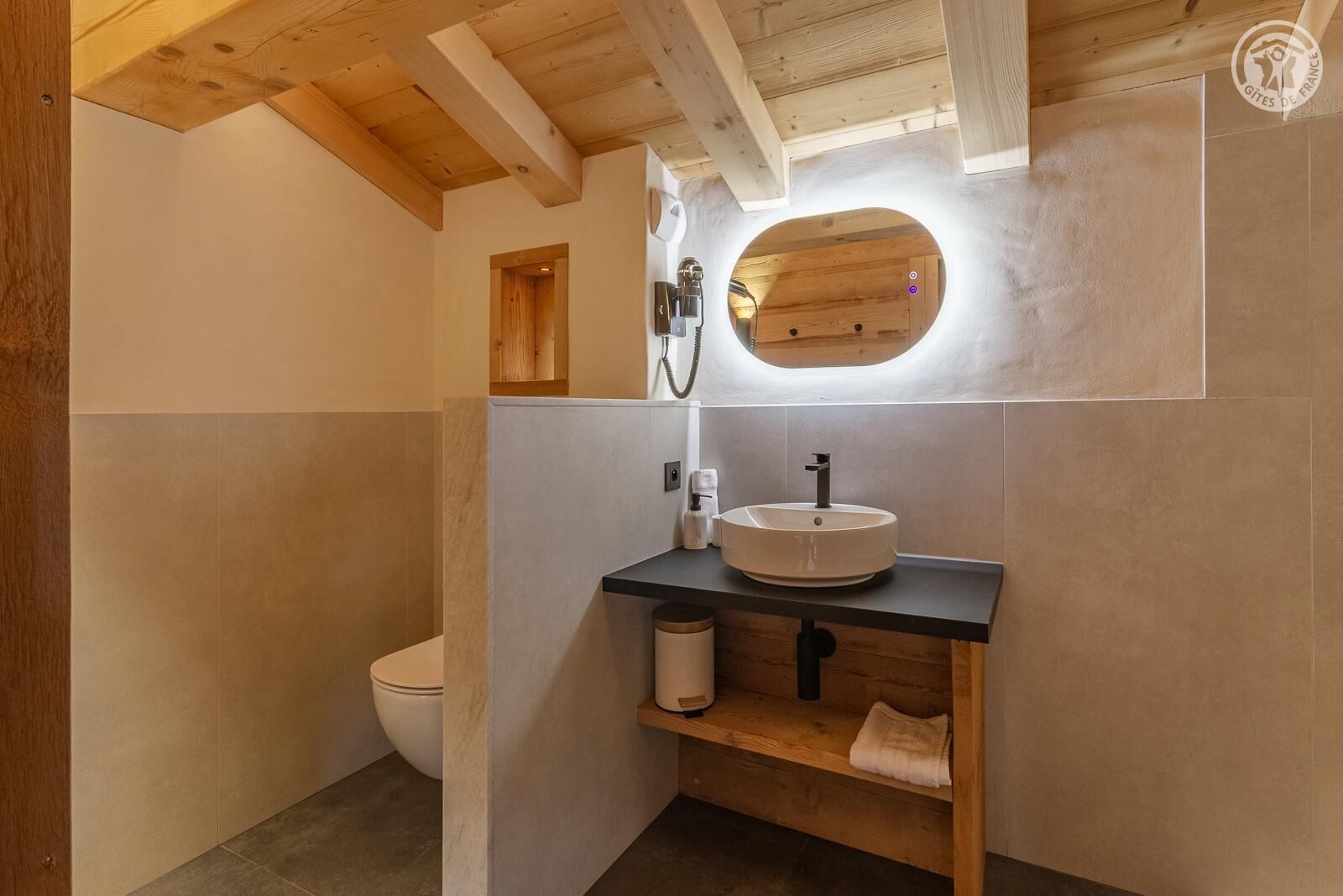 A modern bathroom with a wooden ceiling, a round mirror, a sink, and a toilet.