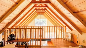 Um quarto no sótão com teto de madeira, janela, ventilador e cama.