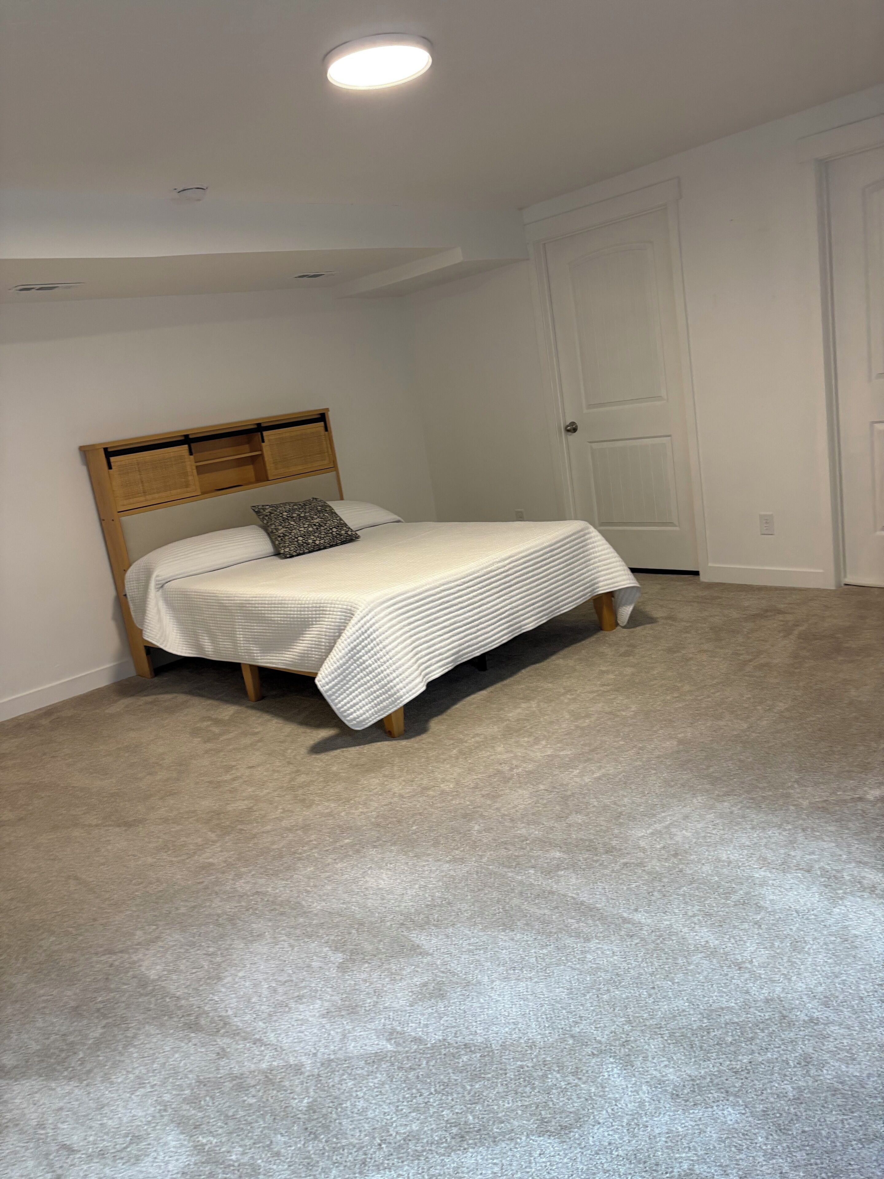 Ein Schlafzimmer mit Bett, Kopfteil, einer Tür und Teppichboden.