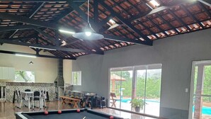 A pool table with balls, a ceiling with wooden beams, and a view of the outdoors. - Sitio toa toa 2 (São roque)