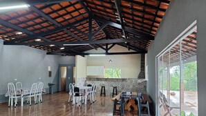 A spacious indoor area with a high ceiling, a dining table with chairs, a kitchen area, and large windows. - Sitio toa toa 2 (São roque)