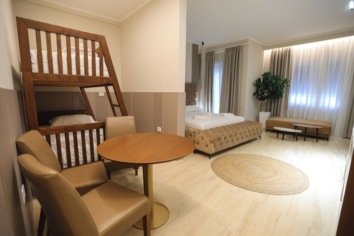 A modern hotel room with a bunk bed, a round table, a sofa, and a large potted plant.