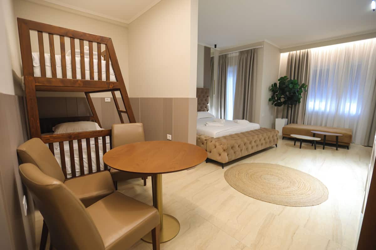 A modern hotel room with a bunk bed, a round table, a sofa, and a large potted plant.