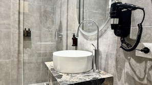 Un baño con un lavamanos redondo, un espejo, un secador de pelo y un dispensador de jabón.