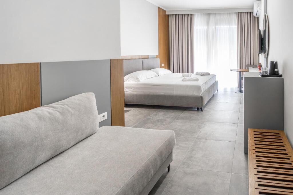 Quarto de hotel moderno com sofá, duas camas, escrivaninha e televisão.