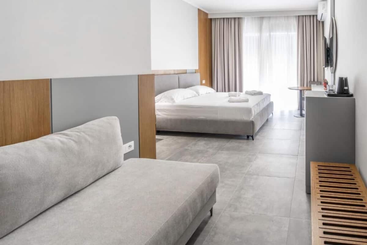A modern hotel room with a sofa, two beds, a desk, and a TV.