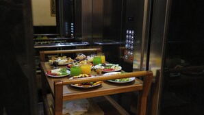 Un bufé de desayuno con diversos platos y bebidas, situado en un moderno hotel con un ascensor visible.