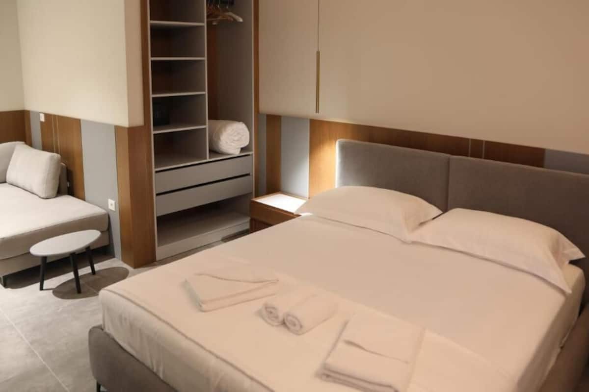 A modern hotel room with a bed, a seating area, and a walk-in closet.