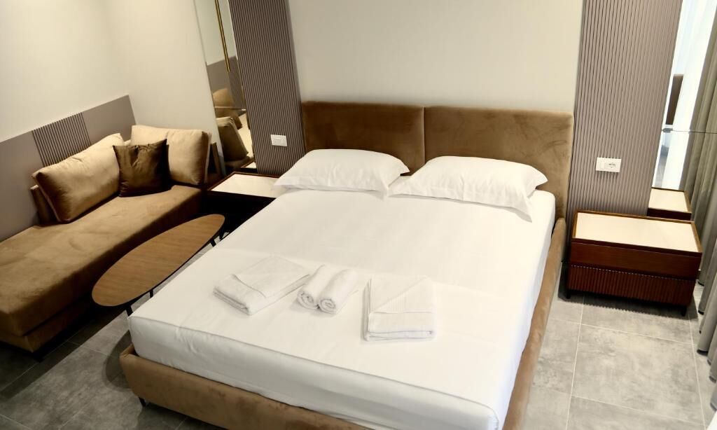 Quarto de hotel com cama, sofá, mesa de cabeceira e espelho.