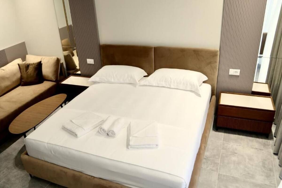 A hotel room with a bed, a sofa, a nightstand, and a mirror.