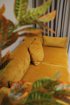 Una cama con cabecera amarilla y almohadas, rodeada de grandes hojas verdes.