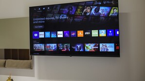 Televisor de pantalla plana montado en una pared que muestra una interfaz de servicio de streaming con diversas categorías de contenido.