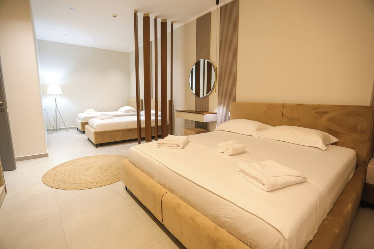 A modern hotel room with a large bed, a bedside table, a mirror, and a separate seating area with a sofa and a lamp.