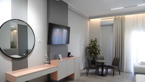 Una habitación de hotel moderna con una televisión de pantalla plana, un espejo redondo, un escritorio, un área de comedor y una cama.