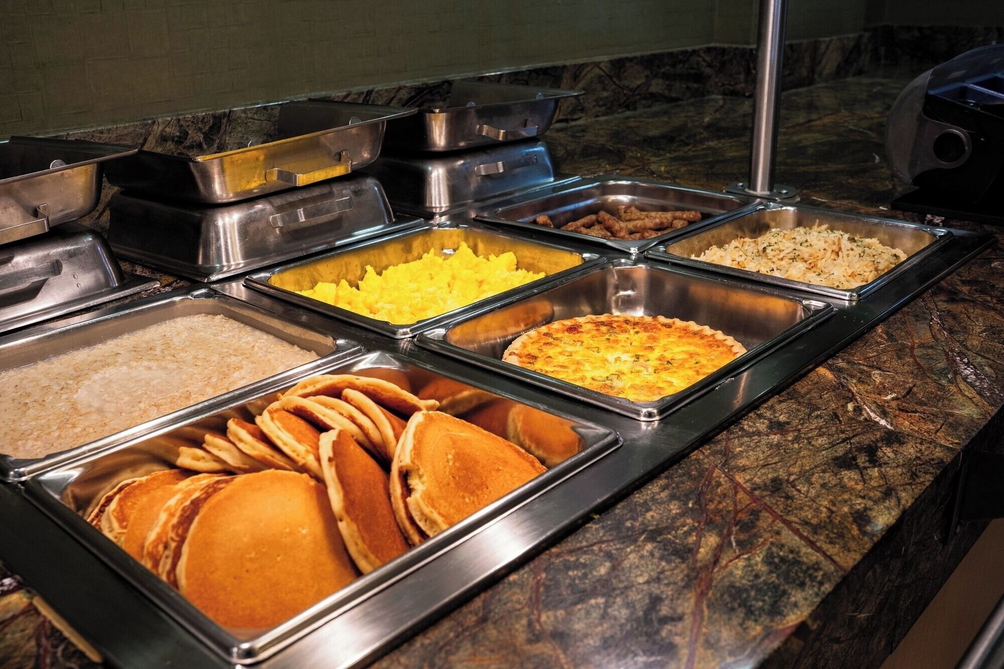 Ein reichhaltiges Buffet mit verschiedenen Speisen, darunter Pfannkuchen, Rührei und Quiche.