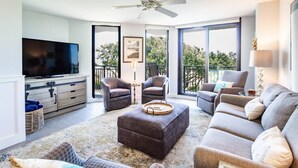 Ein Wohnzimmer mit Flachbildfernseher, zwei Sesseln, einer Couch, einem Couchtisch und einem Balkon mit Blick.