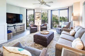 Ein Wohnzimmer mit Flachbildfernseher, zwei Sesseln, einer Couch, einem Couchtisch und einem Balkon mit Blick.