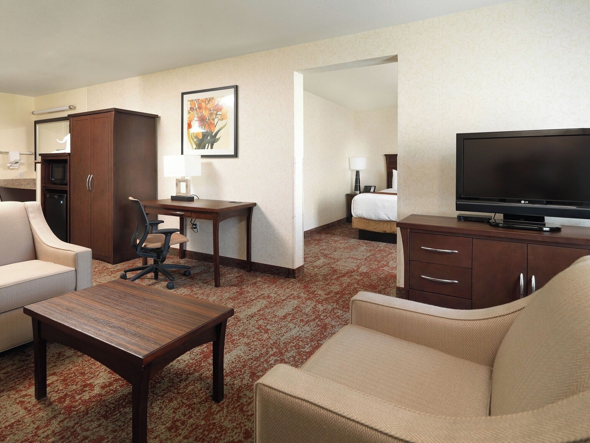 A hotel room with a bed, a TV, a desk, a chair, a sofa, and a cabinet.