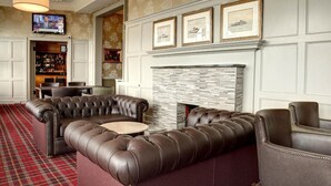 A lounge area with a leather sofa, a fireplace, and a television mounted on the wall. - Best Western Argyll Hotel (Dunoon)