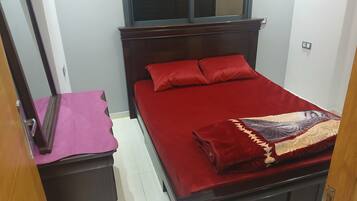 A bedroom with a bed, a nightstand, a dresser, and a window.