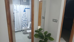 Une salle de bain avec des toilettes, un rideau de douche, une plante en pot et un miroir.
