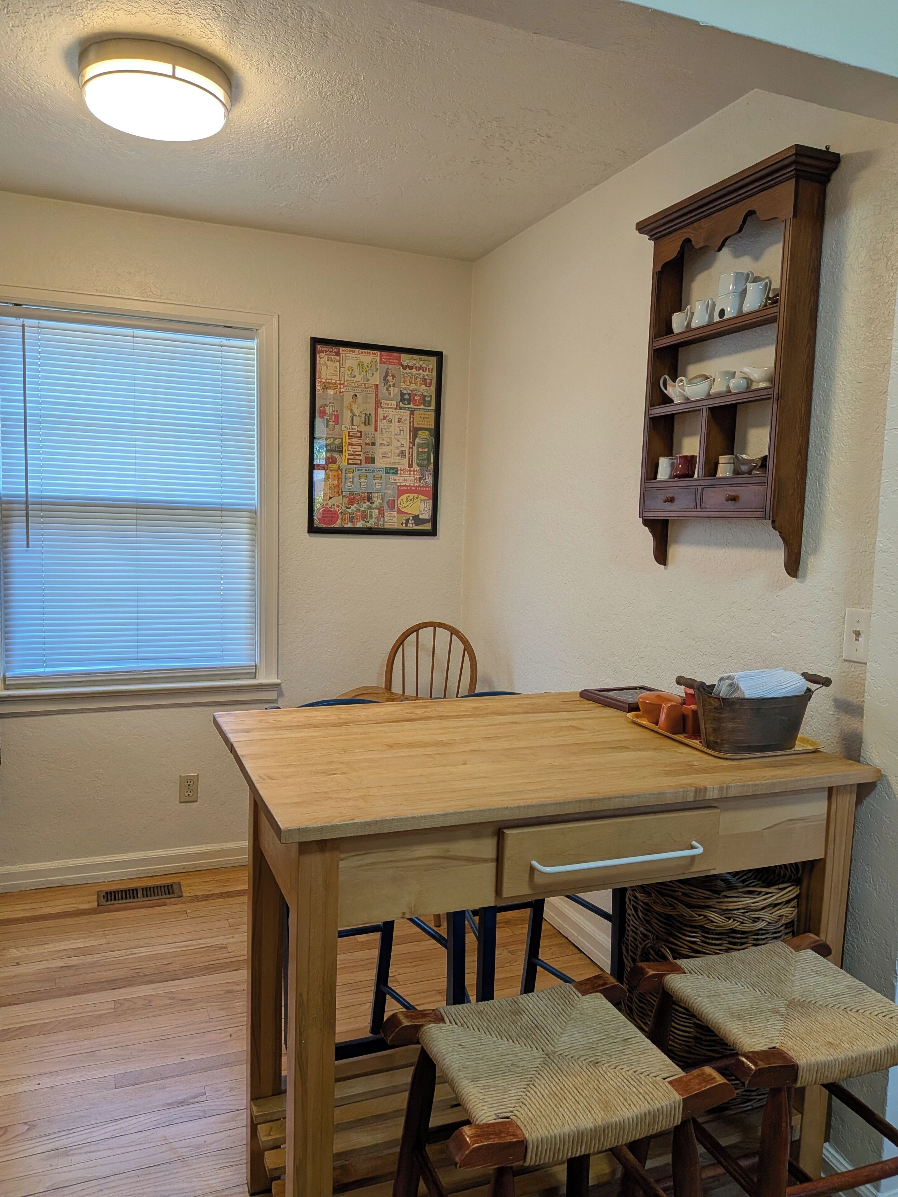 Un coin repas avec une table et des chaises en bois, un tableau d’affichage et une étagère où sont rangés de la vaisselle.