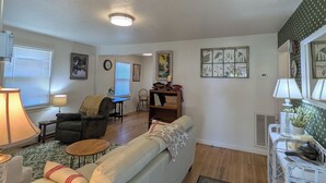 Una sala de estar con sofá, una mesa de centro, lámpara, sillón y estantería.