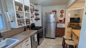 Una cocina moderna con armarios blancos, electrodomésticos de acero inoxidable y un comedor con taburetes de madera.