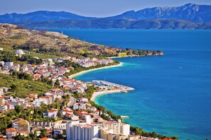 Eine Küstenstadt mit Gebäuden entlang der Uferlinie, blauem Meer und Bergen im Hintergrund.