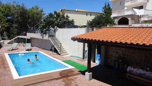 A swimming pool with two people, a covered patio, and a two-story building with balconies. - Holiday apartment with shared pool (Stanići)